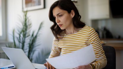 Woman reviewing paperwork on laptop