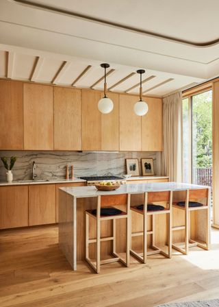 Wood flooring with wooden cabinets and a kitchen island. Marble backsplash has been used in the kitchen as well as the worktops in the space. Two lights hang above the island.