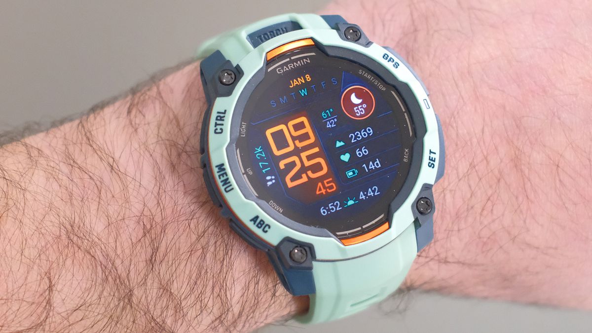 Close up of Garmin Instinct 3 GPS smartwatch in Neotropic/Twilight with a grey and orange case and sea foam green strap