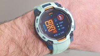 Close up of Garmin Instinct 3 GPS smartwatch in Neotropic/Twilight with a grey and orange case and sea foam green strap