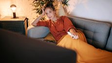 Women dressed in orange watching tv on the couch covered in a blanket