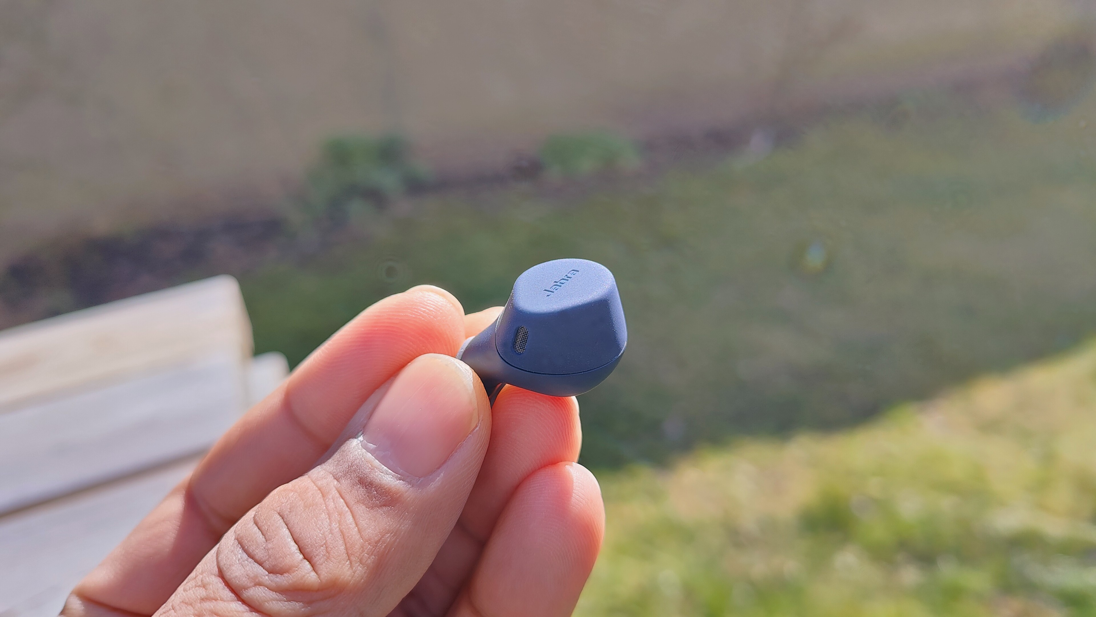 A hand holding Jabra Elite 7 Active outdoors