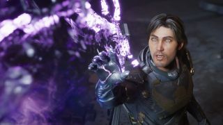 A dark haired man in a sci-fi outfit reaches out to touch a purple alien plant.