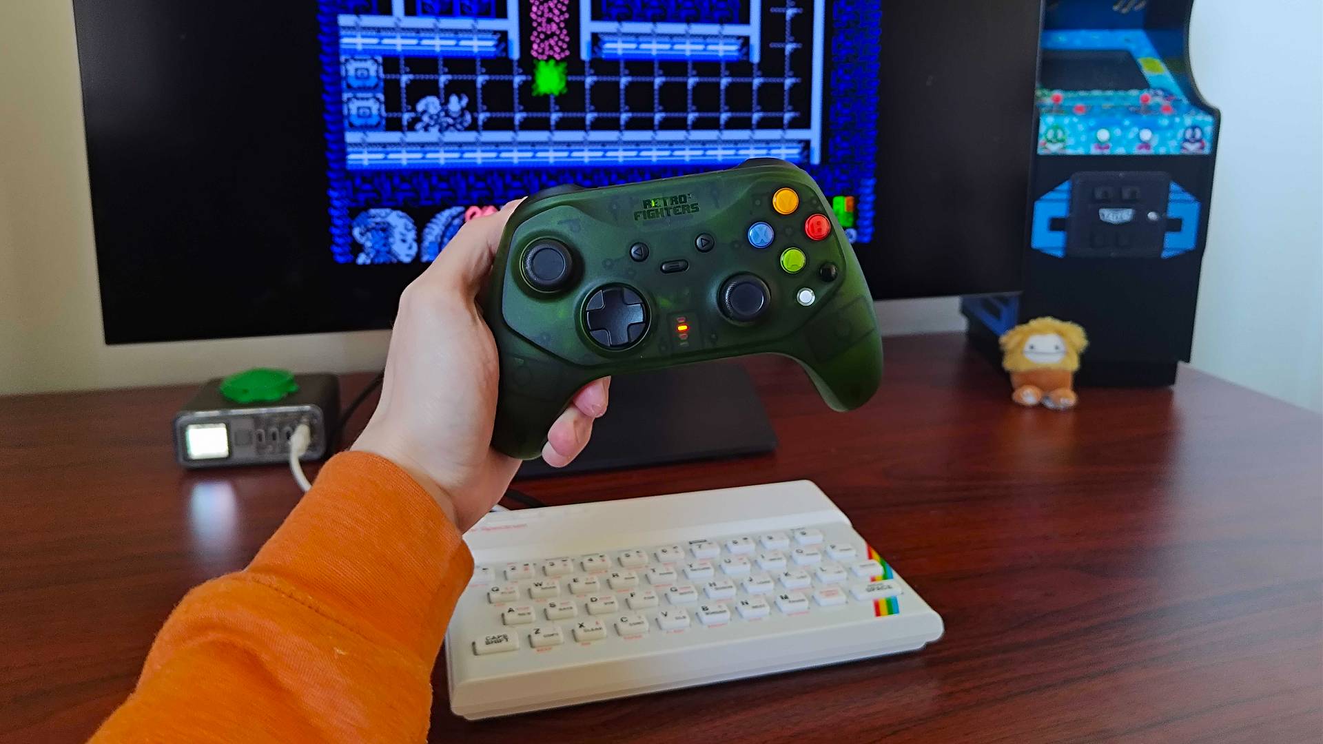 Hand holding Retro Fighters Hunter Xbox controller in front of The Spectrum with Alien Girl running on monitor.