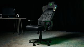 The Razer Soma Chroma chair in an industrial setting, illuminated with a green glow and with a gaming setup in the background