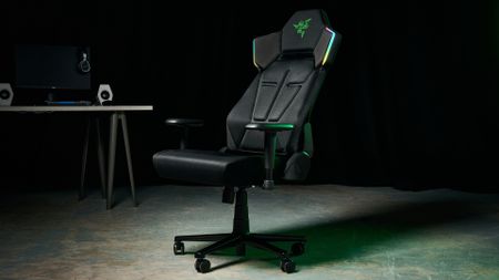 The Razer Soma Chroma chair in an industrial setting, illuminated with a green glow and with a gaming setup in the background
