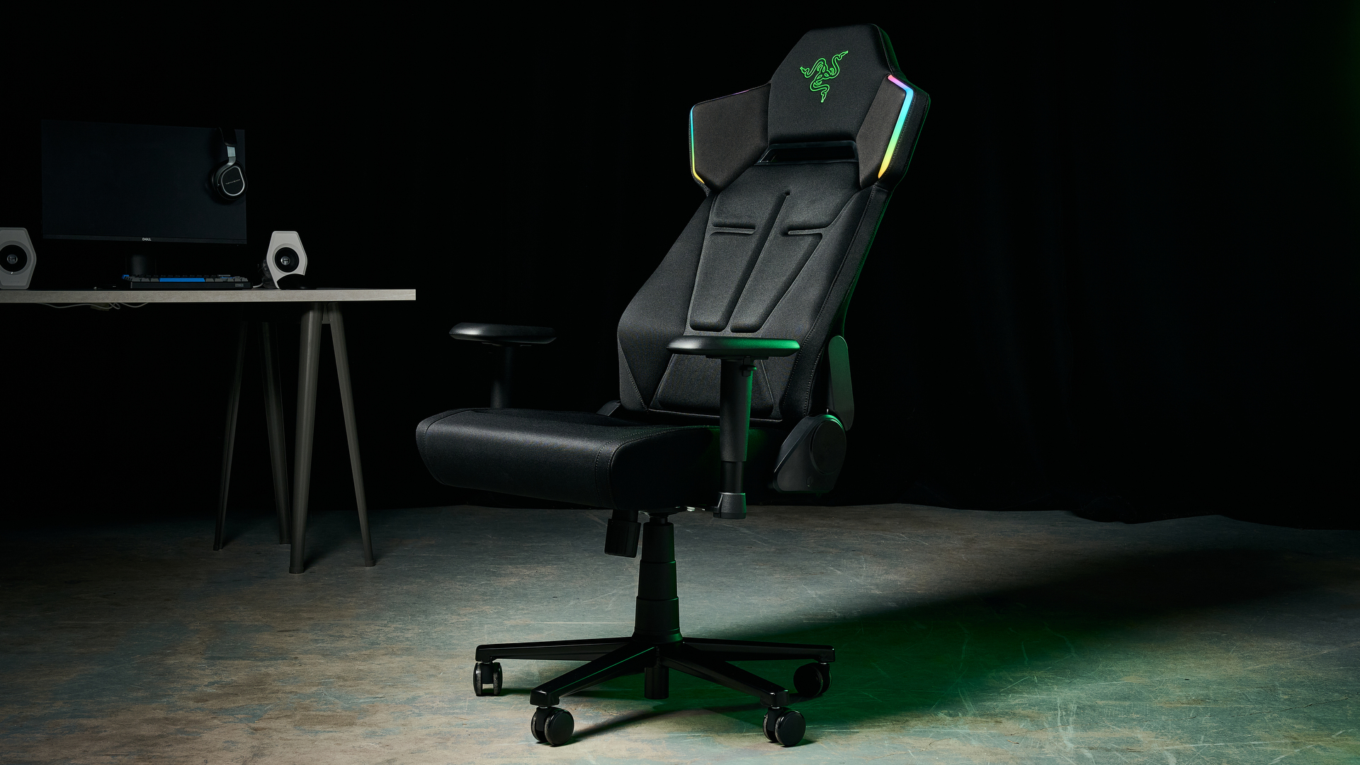 The Razer Soma Chroma chair in an industrial setting, illuminated with a green glow and with a gaming setup in the background