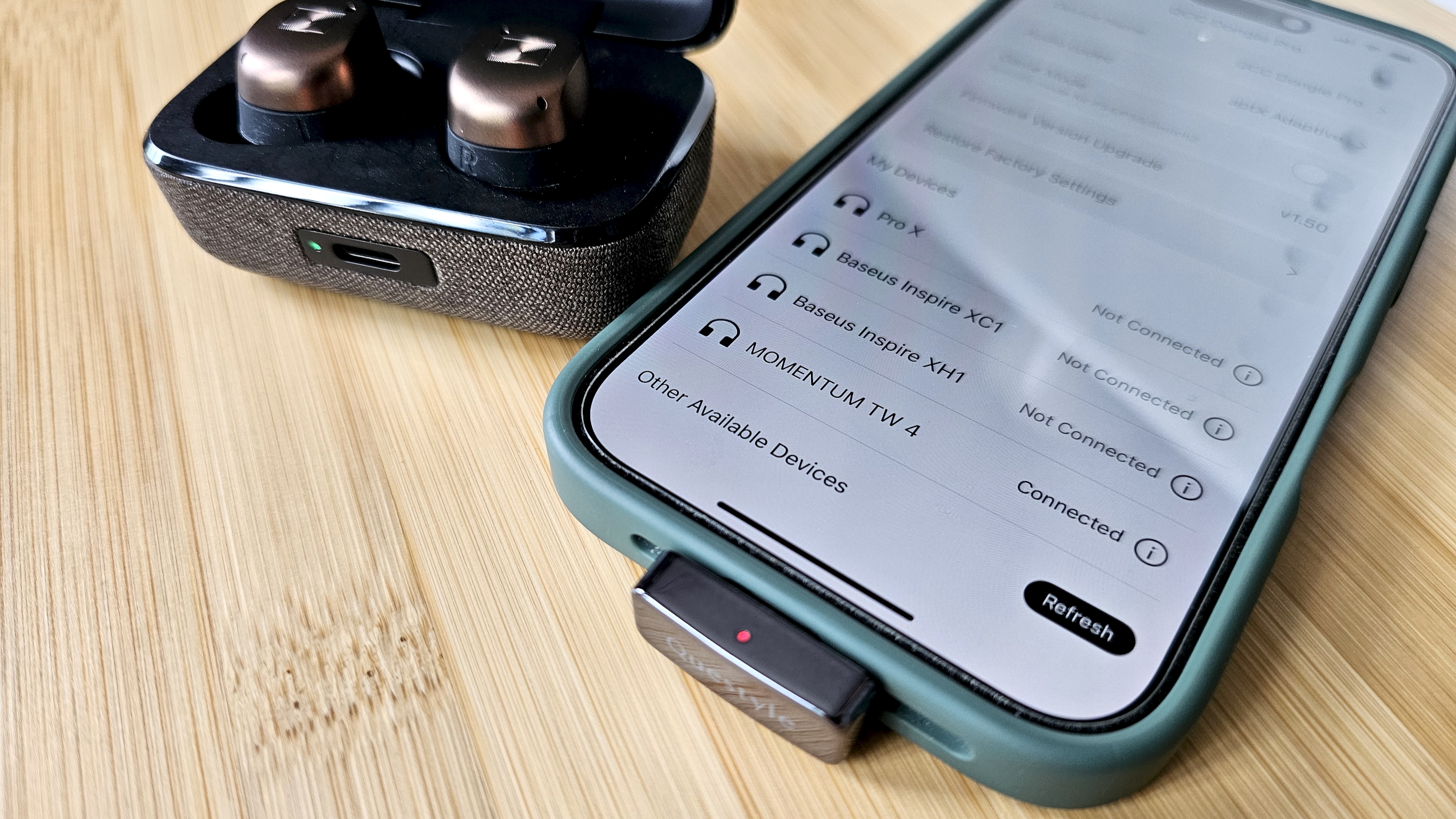 The Questyle QCC Dongle Pro with a smartphone to denote size, on a light wooden table