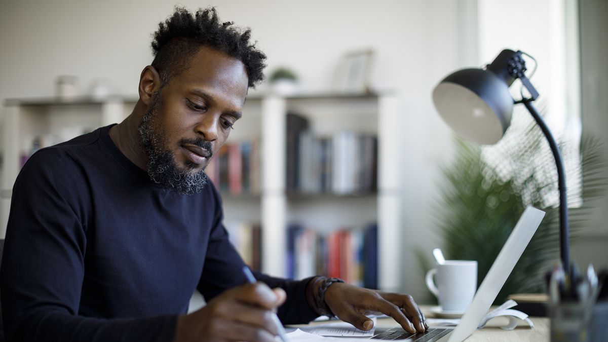 A businessman taking notes on a pad of paper while working on a computer