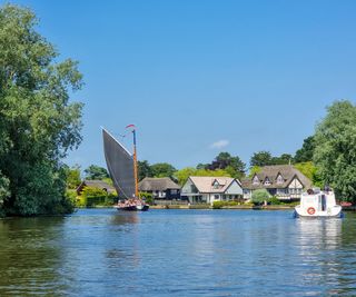 Norfolk Wherry sails past riverside houses in Norfolk Broads