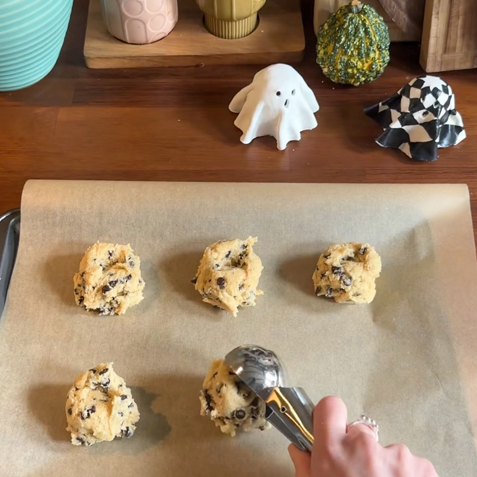 Person using ice cream scooper to put balls of cookie dough onto parchment paper