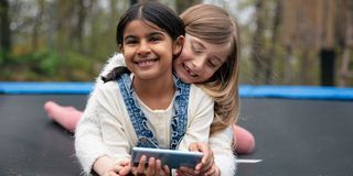 To barn på en trampoline med en mobiltelefon.