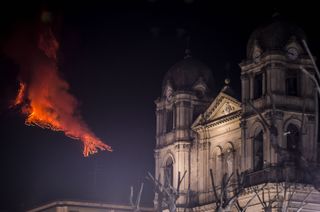 A church in Catania, Italy stands undisturbed as Mount Etna erupts miles away.