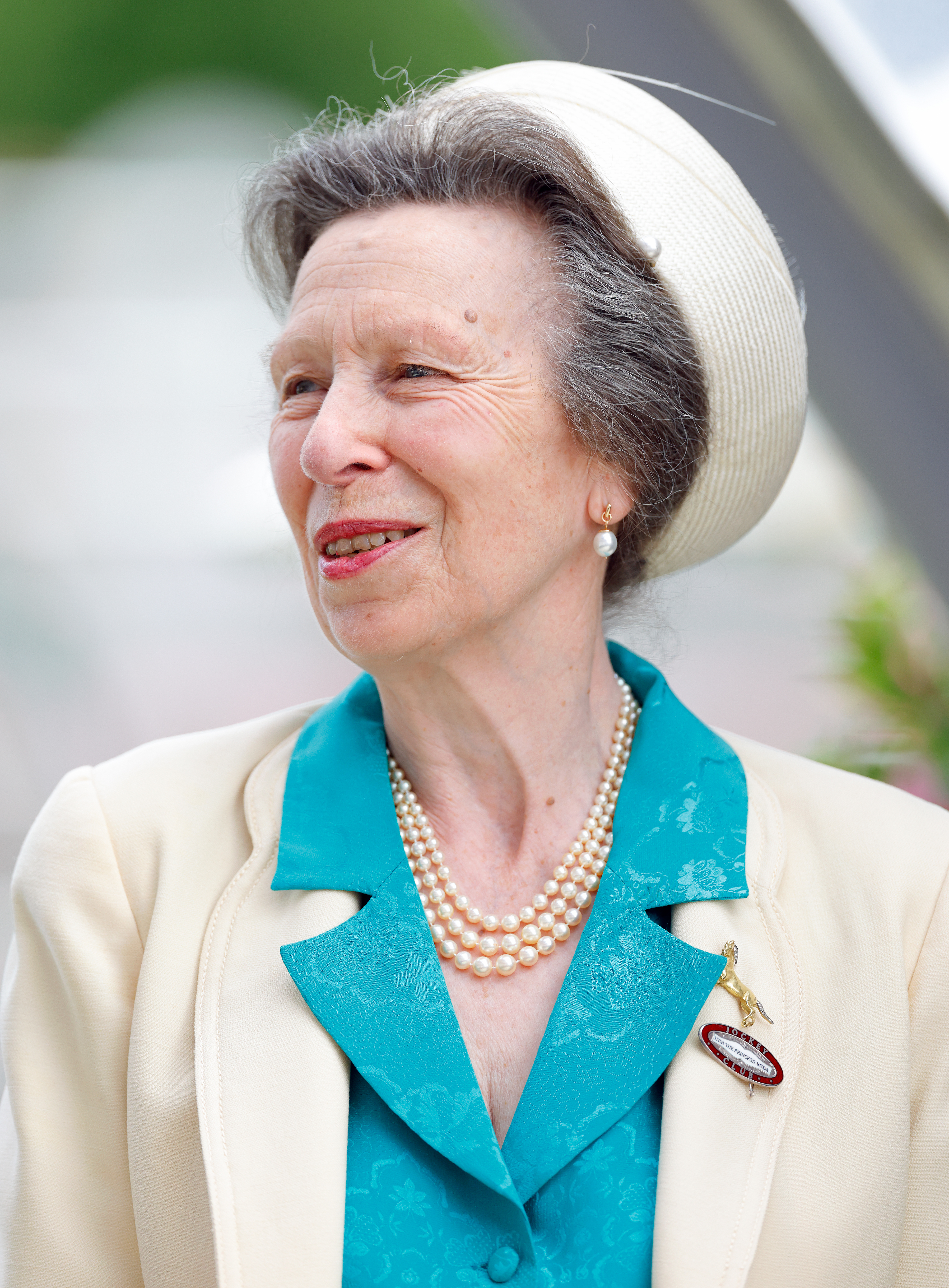 Princess Anne smiling in a pillbox hat and pearls