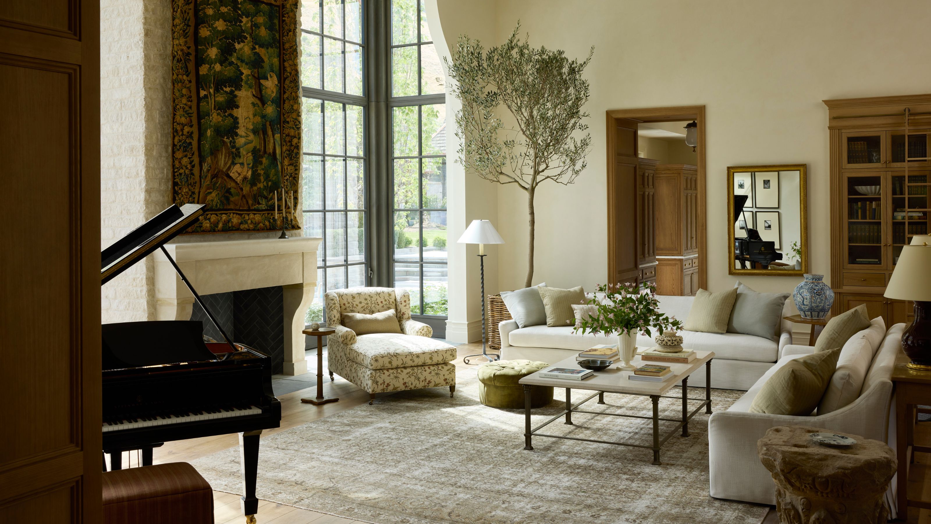 a vast Great Room in Utah with large glass wall to floor windows, stone fireplace with a tapestry above, a piano, and cozy sitting area