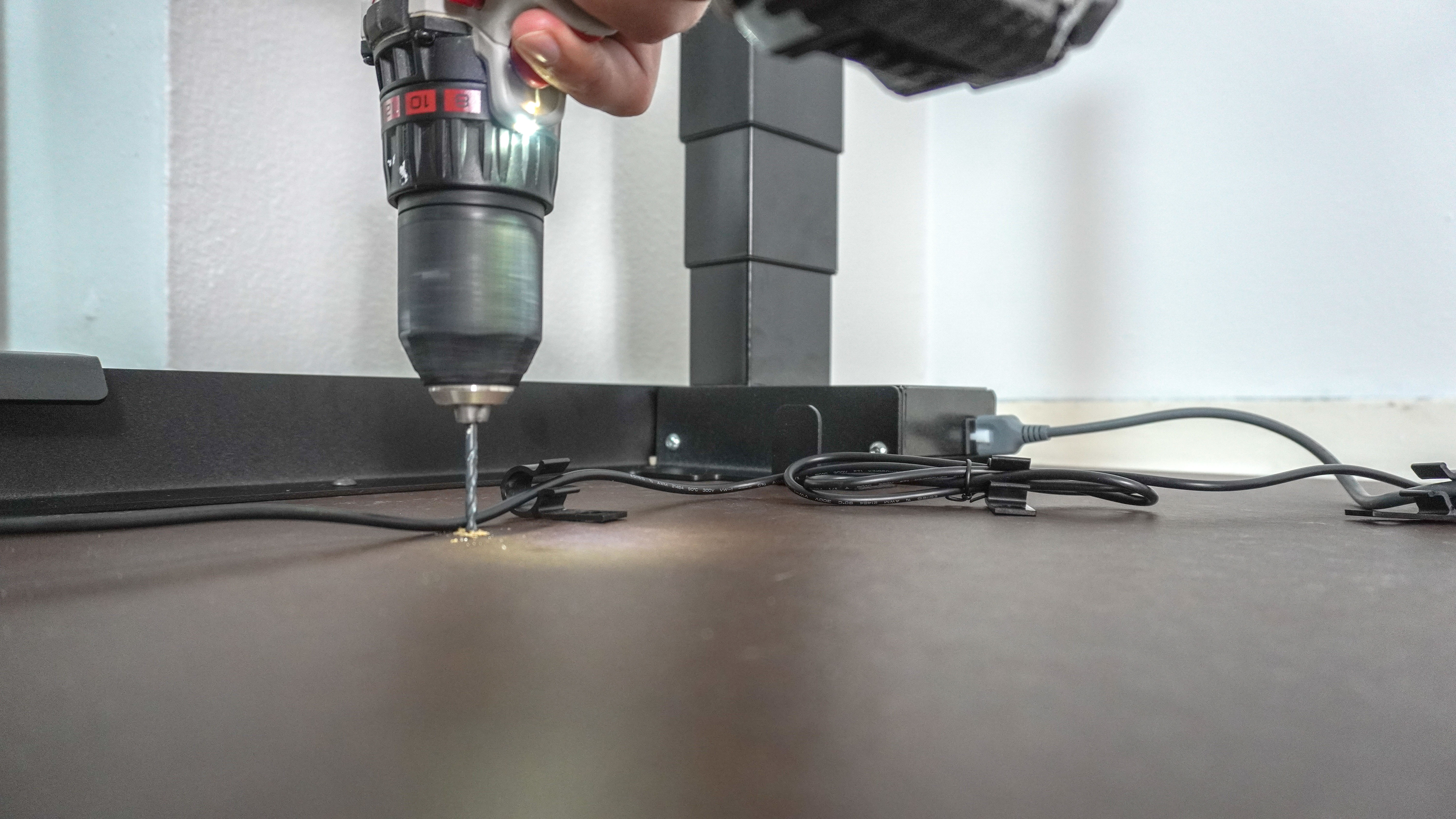 A person drilling pilot holes into the Herman Miller Coyl Gaming Desk to install cable management clips