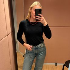 Woman wears black long-sleeved top, red bead necklace, blue jeans