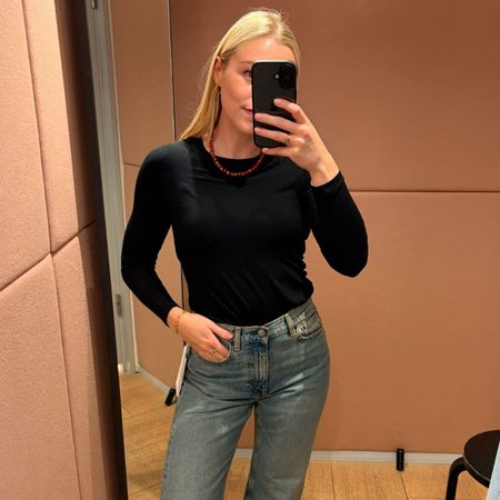 Woman wears black long-sleeved top, red bead necklace, blue jeans