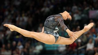 A female gymnast jumps through the air doing the splits with her back arched