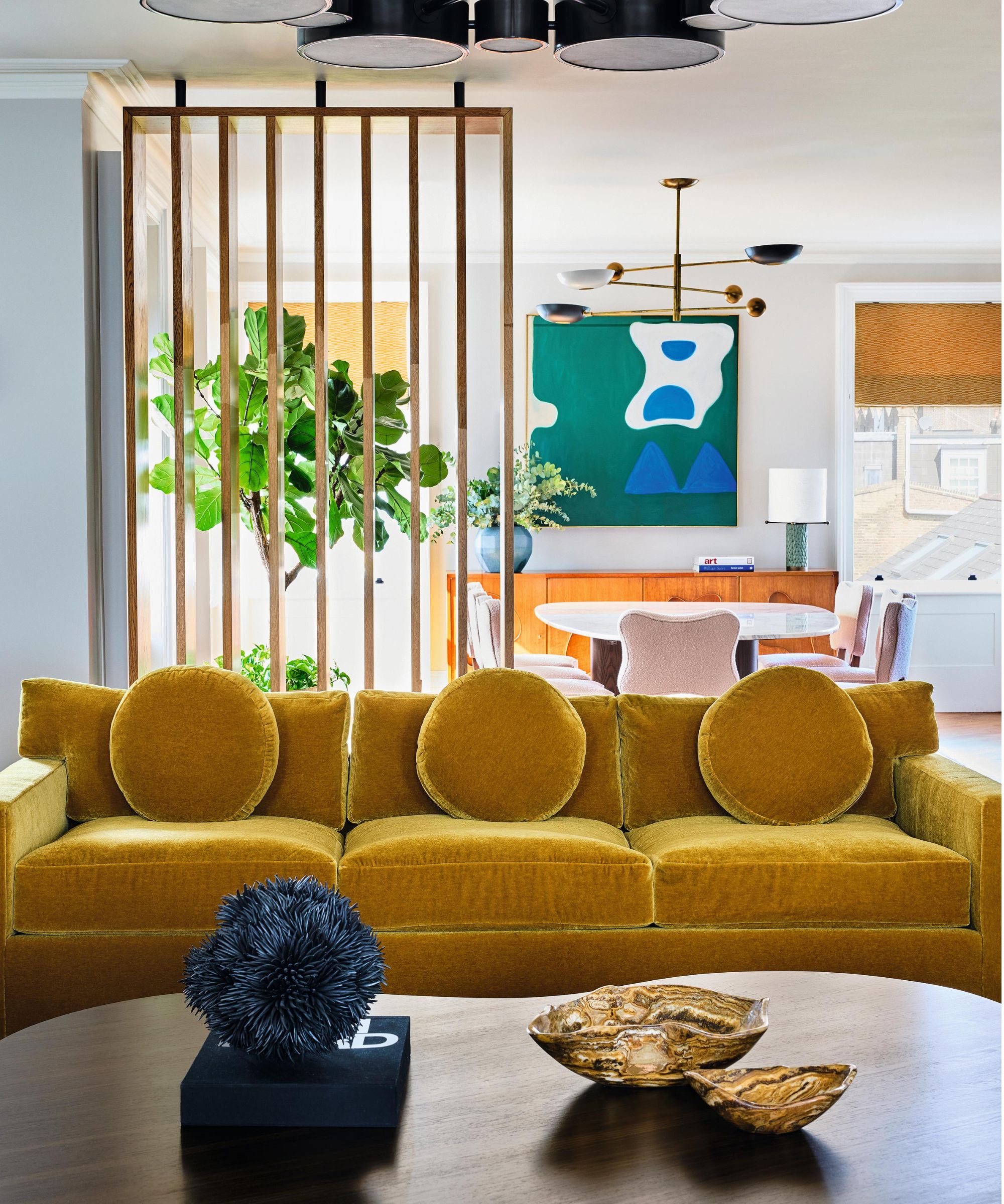 a white living room with wooden dividers, wooden coffee table, mustard velvet couches and abstract art and decor