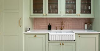 Sage green kitchen cabinets with pink splashback and gold handles