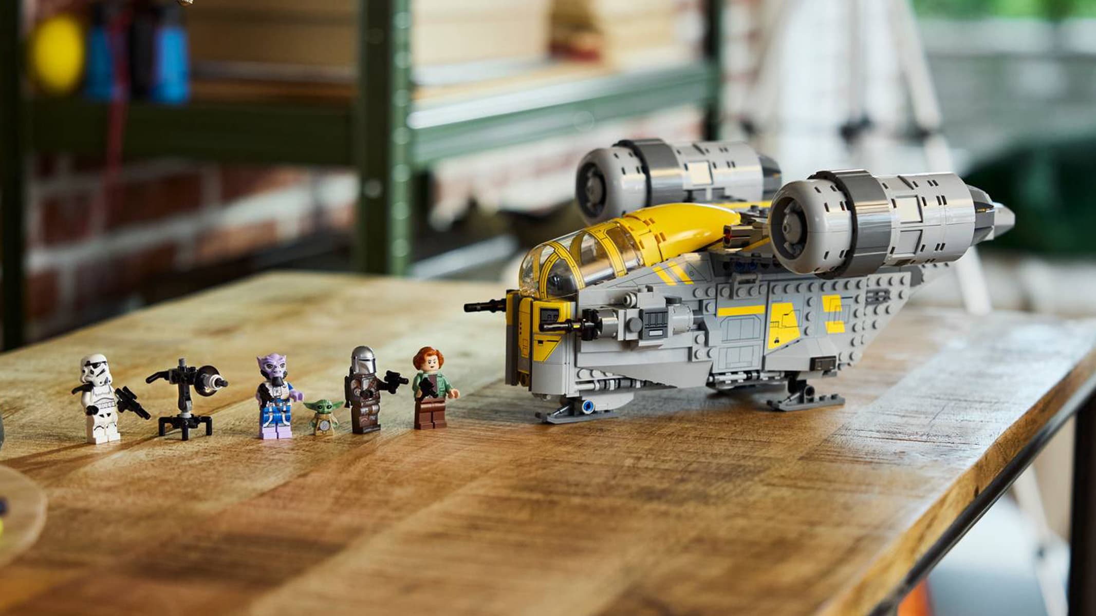 A brick-built gray and yellow space ship is displayed on a brown wooden table along with minifigures