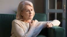 An older woman looks pensive as she sits on her sofa.