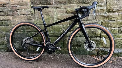 The Whyte Tourus bike in black lent up against a stone wall