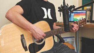 A man records acoustic guitar with a condenser microphone