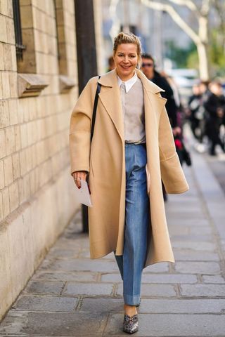 A street style influencer wearing a camel coat with blue jeans