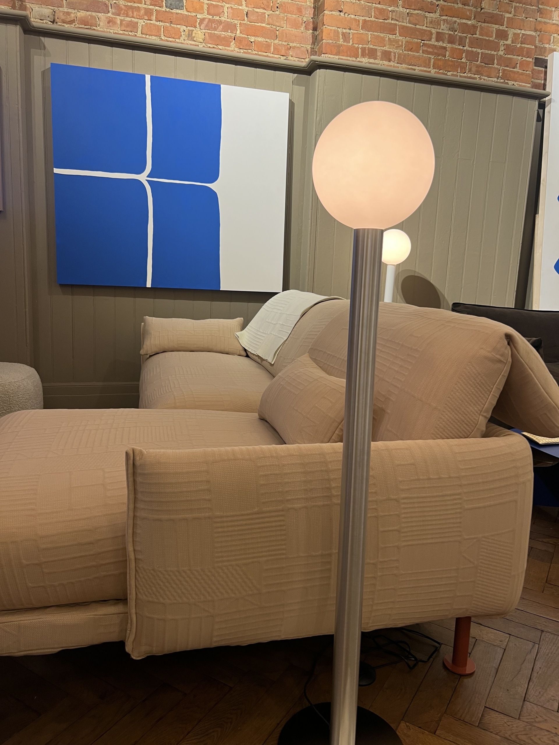 Image of a textured, pale peach Cozmo sofa with a floor lamp next to it that has a metal stand and a bulb light