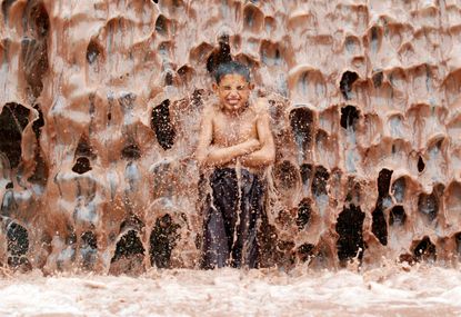 An Afghan boy cools off under a muddy waterfall.