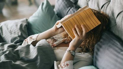 A woman lying in bed with a book over her face