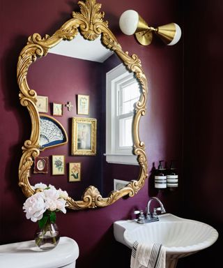 Dark purple bathroom with ornate golden mirror, golden wall light
