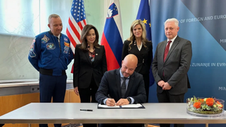 a group of people stand behind a man signing a document in front of flags
