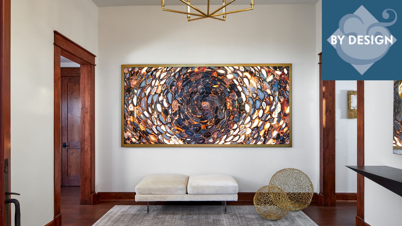 Modern entryway with large crystal artwork on back wall, bench, rug and two metal sculptures below, wooden flooring and door frames surrounding