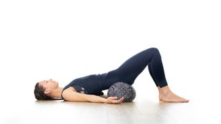 woman in bright white yoga studio, lying on bolster cushion
