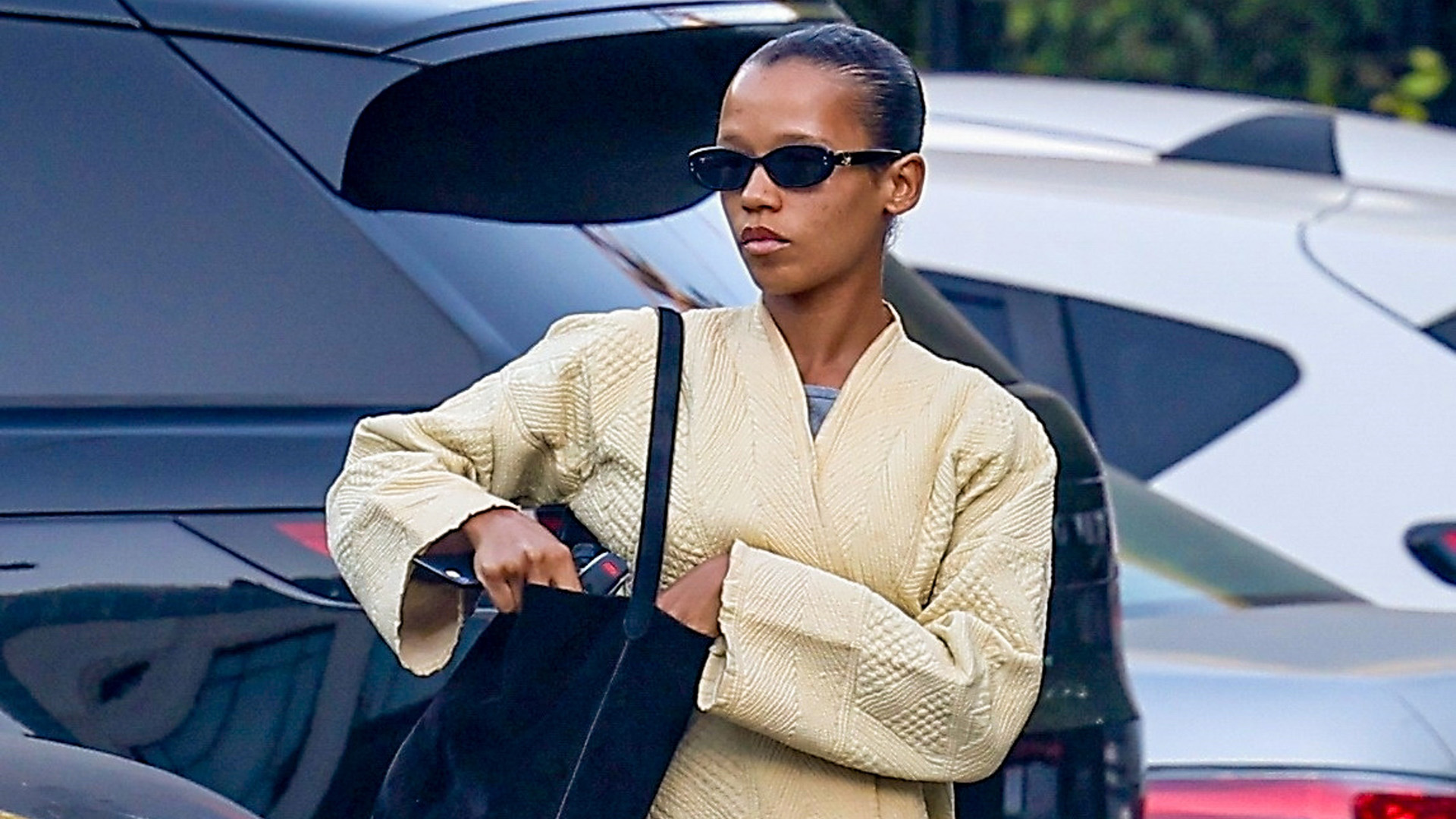 Taylor Russell wearing a butter yellow wrap coat with gray leggings and jelly flip-flops.