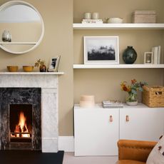 Beige living room with open fire and a white marble fireplace, and white cupboards in the alcoves