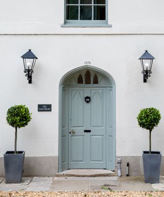 white stone house with blue front door and bay trees