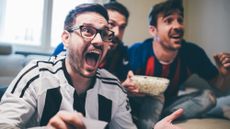 Men shouting in excitement and eating popcorn while watching sports game together