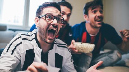Men shouting in excitement and eating popcorn while watching sports game together