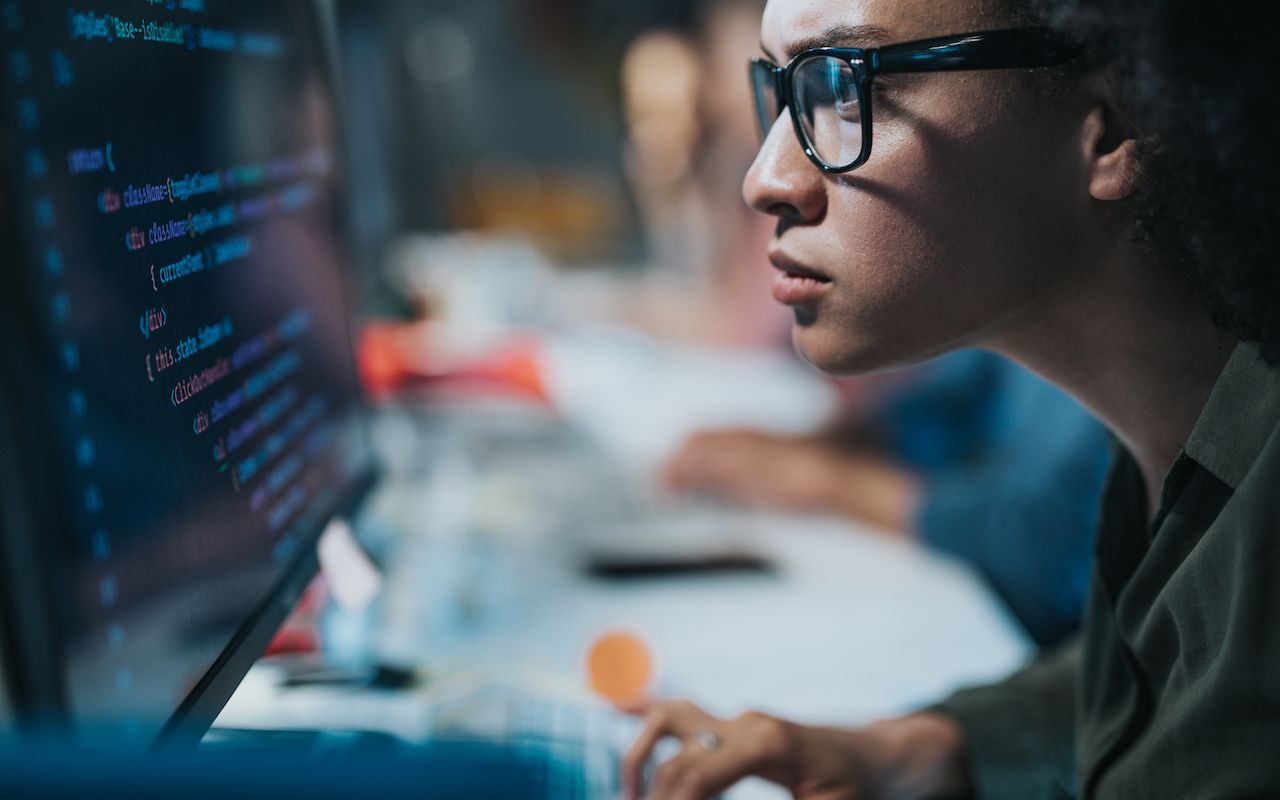 Focused black female programmer coding new computer language while working on desktop PC in the office.