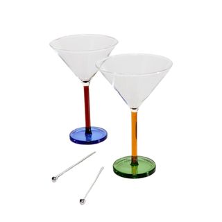 Two glass martini glasses - one with a red stem and blue base and one with an orange stem and green base - with two glass stirrers in between them