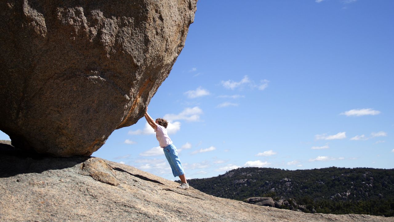 A very small person appears to be pushing a large boulder up a rocky hill.