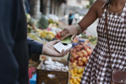 A woman in a colorful outdoor market taps her credit card on a merchant's mobile card reader.