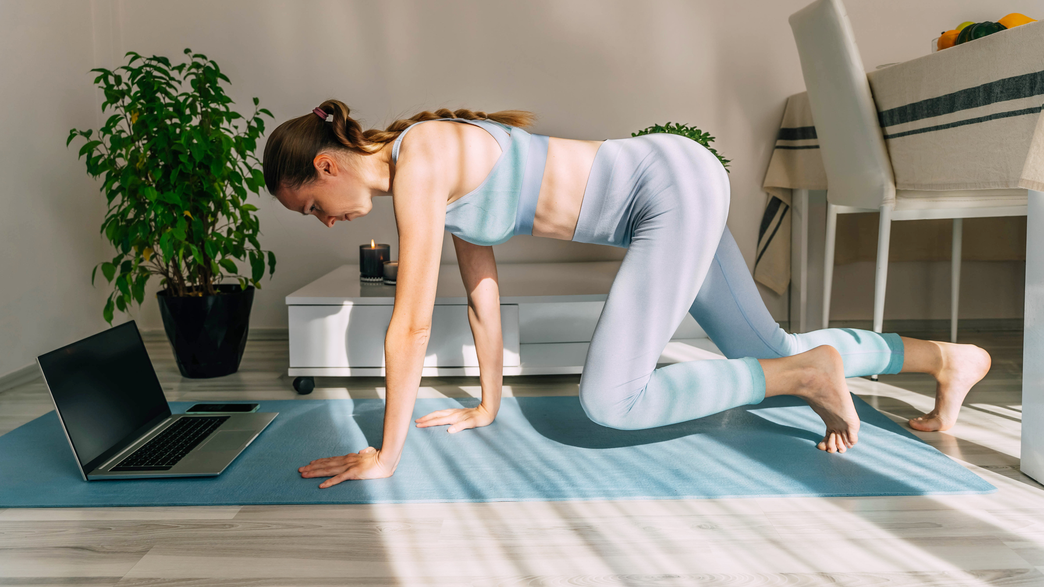 Woman performing bear crawl in domestic setting with laptop on the exercise mat in front of her