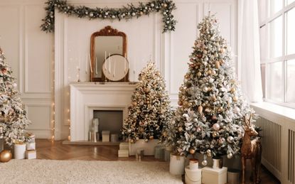 Living room in light off-white with fireplace and two christmas trees by the windows and gifts