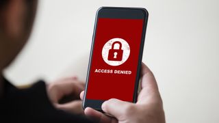 A man holding a smartphone displaying the message "access denied" in white lettering on a red background