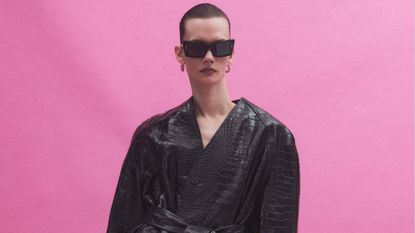 Model in black mac by Balenciaga and sunglasses on pink background